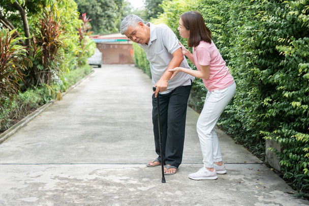 Aasian vanhempi mies kävelee takapihalla ja kivulias tulehdus ja jäykkyys nivelten (niveltulehdus) ja tytär tuli auttamaan tukea. Vanhan vanhusvakuutuksen ja terveydenhoidon käsite - Valokuva, kuva