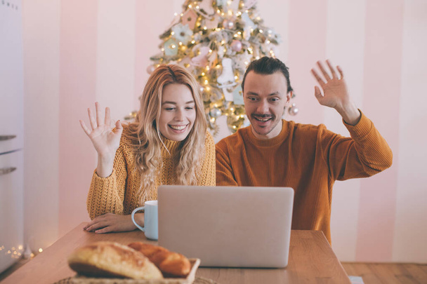 Szczęśliwa młoda para wykonująca połączenie wideo z laptopem, witając swoją rodzinę świętami Bożego Narodzenia lub Nowego Roku. - Zdjęcie, obraz