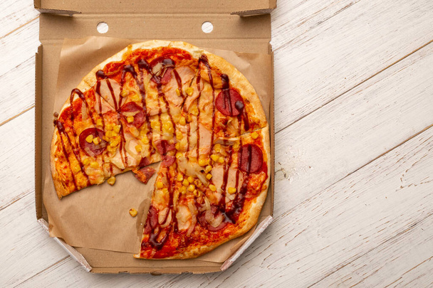 Pizza in a cardboard box on a white wooden background. - Fotoğraf, Görsel