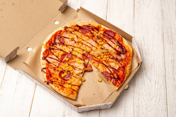 Pizza in a cardboard box on a white wooden background. - Foto, afbeelding