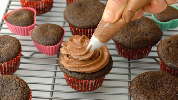 Versieren chocolade cupcakes met chocolade boterroom glazuur met behulp van een gebak zak, close-up voorbereiding - Foto, afbeelding