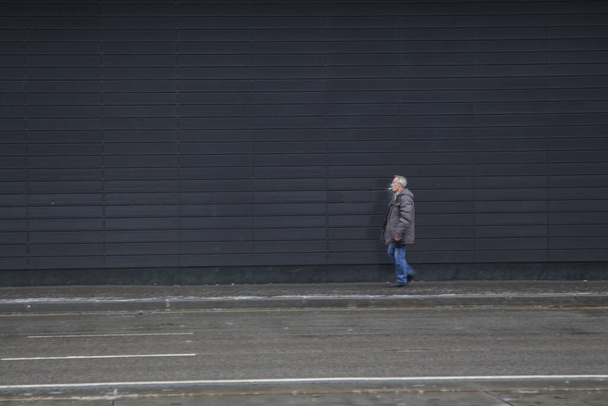 Москва (Росія) 21 листопада 2020 року: чоловік іде по вулиці Вавілову вздовж тротуару через темну стіну торгового центру. - Фото, зображення