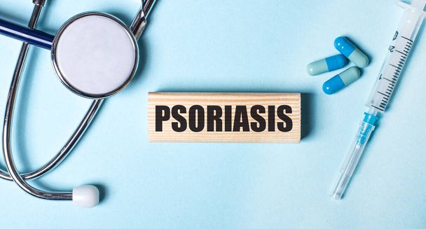 On a blue background, a stethoscope, a syringe and pills and a wooden block with the word PSORIASIS. Medical concept - Фото, изображение