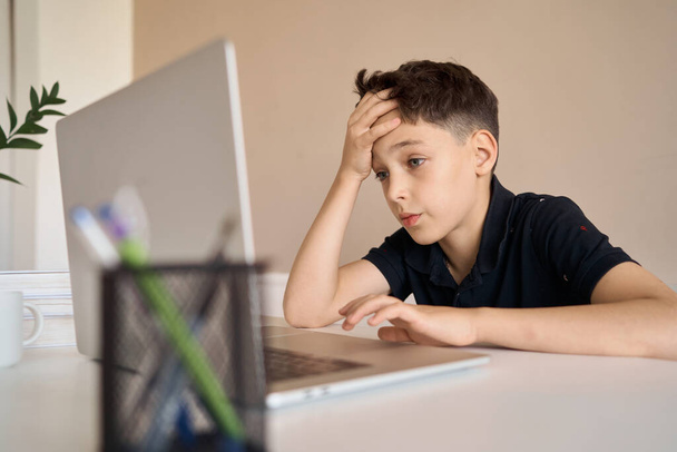 Smart looking boy doing his homework and look at computer notebook at home due to Covid-19 pandemic and social distancing, New normal, Remote class. - Φωτογραφία, εικόνα