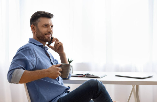 Bonito freelancer homem falando no celular e beber café em casa - Foto, Imagem