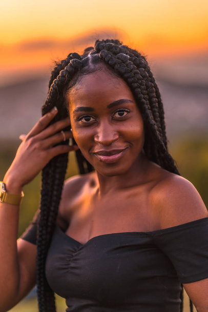 Lifestyle, Latina girl with black skin in a tight black short dress. Portrait of the young man on top of the mountain in a beautiful summer sunset - Fotografie, Obrázek