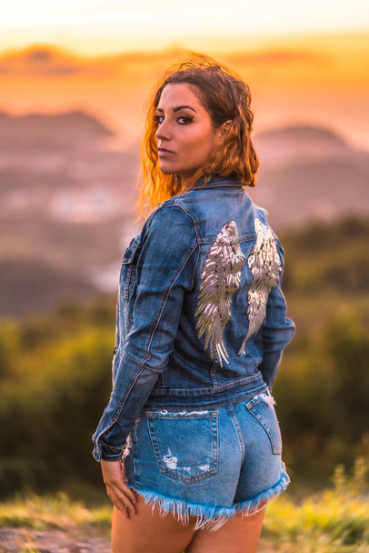 Lifestyle, Caucasian girl in a denim jacket and denim shorts. Portrait in a beautiful summer sunset - Фото, зображення