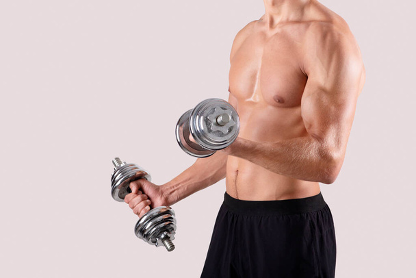 Tuntematon lihaksikas kehonrakentaja, jonka käsipainot pumppaavat lihaksia valoisan studion taustan yli, kopioi tilaa - Valokuva, kuva