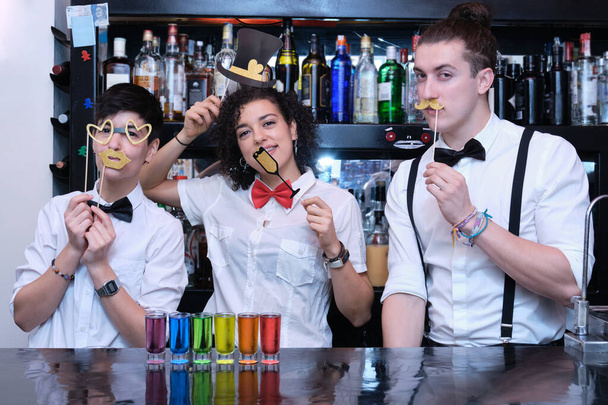 Tres camareros con accesorios festivos y fotos LGBT en un bar. Camareros divertidos y amables con pajarita en un pub. - Foto, Imagen