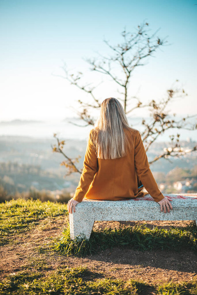 Женщина в жёлтом пальто сидит на скамейке и созерцает пейзаж Виго, Галисия - Фото, изображение