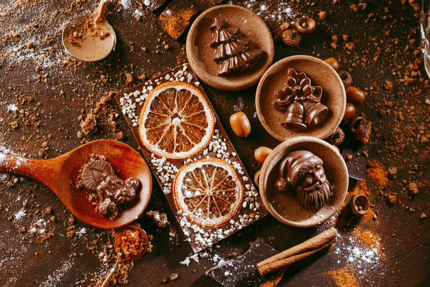 various Christmas figurines made in chocolate lie on a dark background next to Cutlery and spices - Zdjęcie, obraz