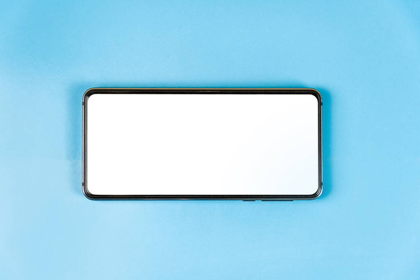 Een smartphone met een plaats voor een inscriptie op wit ligt op een blauwe tafel. Concept voor de ontwikkeling van nieuwe technologieën. Vrije ruimte voor tekst - Foto, afbeelding