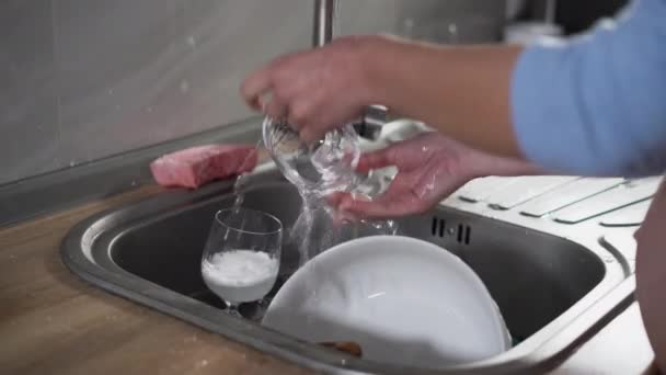 primo piano delle donne mano lava bicchieri e piatti nel lavandino. - Filmati, video