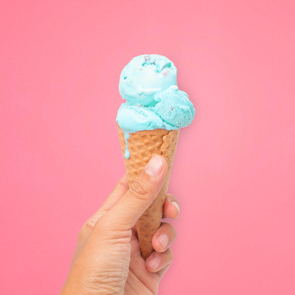 woman hand holding wafer cone with blue  ice cream on pink background - Фото, изображение
