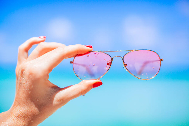 femmes main tenant des lunettes de soleil sur la plage tropicale - Photo, image