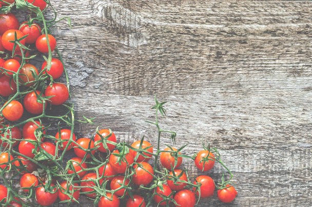 Ripe fresh cherry tomatoes with green branches on a wooden table. Light tint, top view. - 写真・画像
