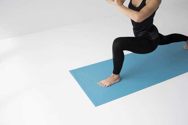 Young woman is practicing yoga in a studio. Slim young girl in a black sport wear is doing yoga practice on a blue mat. Concept of healthy life and natural balance between body and mental development. - Photo, Image