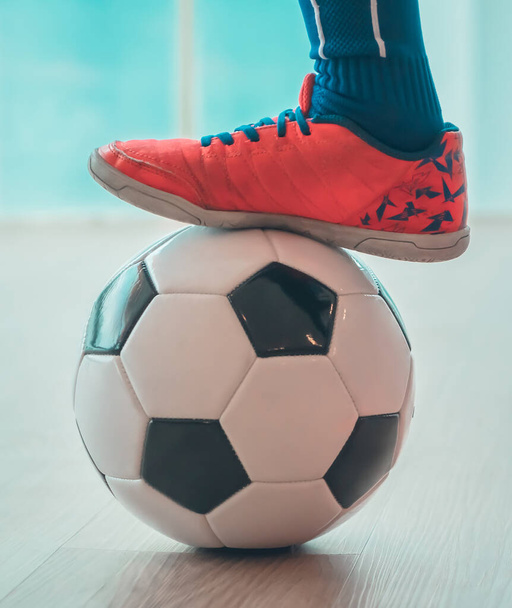 Детские ножки для футбола наступают на футбол для молодёжного спорта в помещении. - Фото, изображение