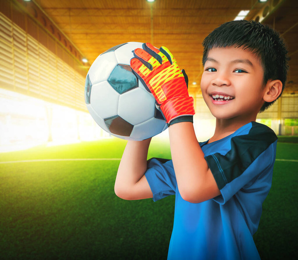 Menino asiático é um goleiro de futebol usando luvas e segurando uma bola de futebol para conceito de esporte juvenil. - Foto, Imagem