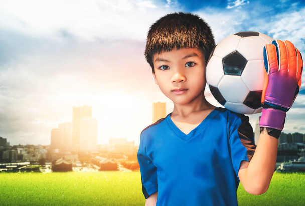 ásia menino é um futebol goleiro vestindo luvas e segurando um futebol bola com cidade fundo copyspace. - Foto, Imagem