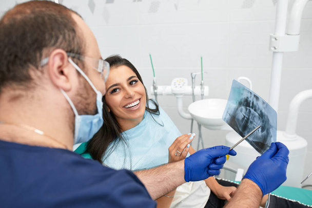 άτομα, ιατρική, στοματολογία και υγειονομική περίθαλψη έννοια - ευτυχισμένη αρσενικό οδοντίατρο δείχνει το πρόγραμμα εργασίας για τη γυναίκα ασθενή στο οδοντιατρείο - Φωτογραφία, εικόνα