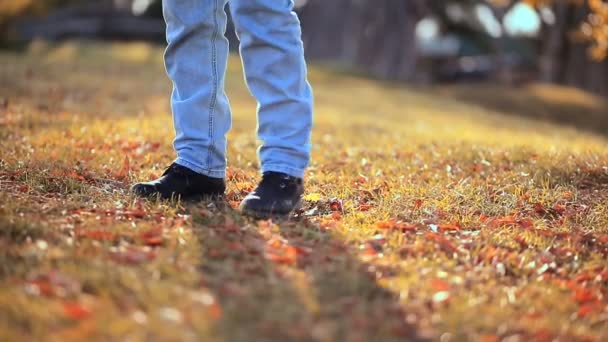Kotlu ve çizmeli biri yaprakları tekmeliyor, bir ayağından diğerine kayıyor. Bacaklar yakın. Arka planda Autumn Park. - Video, Çekim