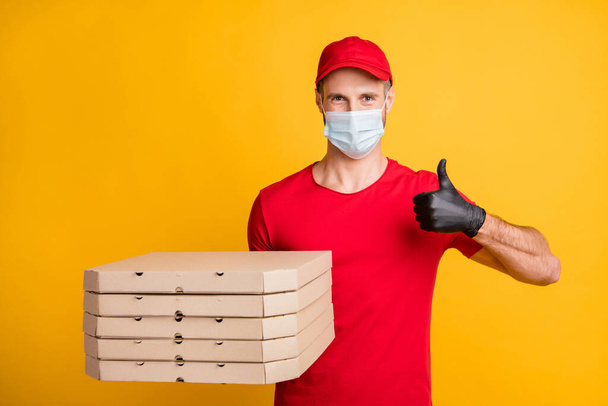 Photo of young courier man hold pizza boxes raise thumb up wear mask red t-shirt cap isolated yellow color background - Fotó, kép
