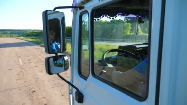 Vrachtwagen in zonnebril reflecteert in zijspiegel van bewegende auto. Man rijden vrachtwagen rijden naar bestemming via het platteland weg. Vrachtvervoer concept. Mooie achtergrond. Slow mo close-up - Video