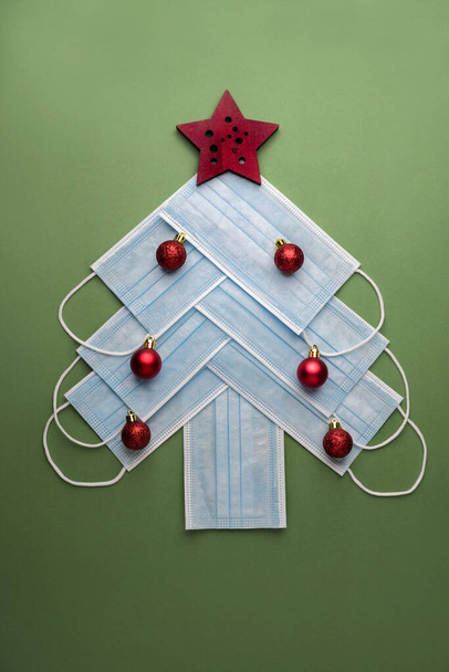 Fondo concepto de Navidad.Máscaras quirúrgicas protectoras en forma de árbol de Navidad sobre fondo verde - Foto, imagen