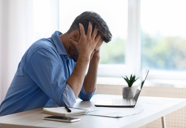 Стресс мужчина фрилансер, сидящий за столом в домашнем офисе, имеющие проблемы с бизнесом - Фото, изображение