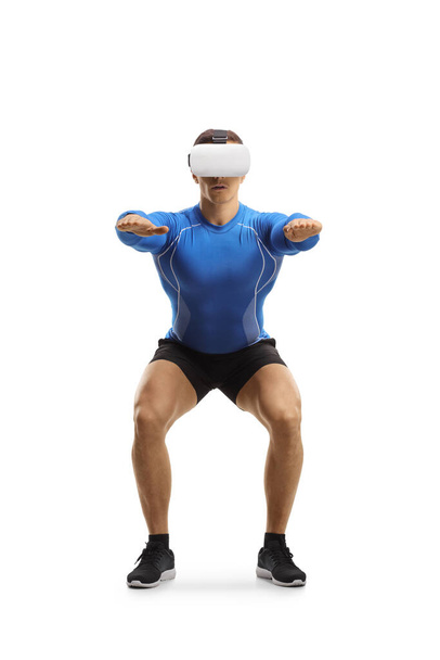 Muscular guy exercising squats with a VR headset isolated on white background - Fotó, kép