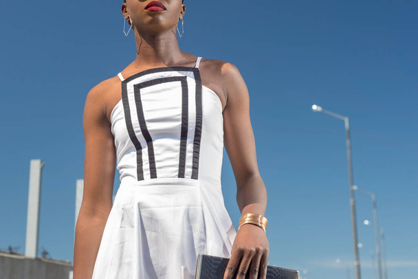 divat afrikai fekete lány fehér ruhában, modell pózol a kék ég hátterében. Fiatal afro-amerikai lány modell fehér ruha nyitott hát pózol ellen kék ég Szexi afro-amerikai nő rövid ruha - Fotó, kép