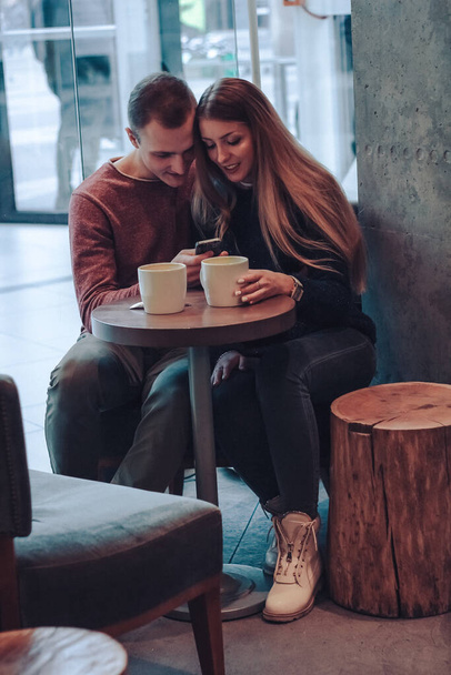Άντρας και γυναίκα πίνουν καφέ σε ένα καφέ. Δύο άνθρωποι, άνδρες και γυναίκες στο καφέ επικοινωνούν, γελώντας και απολαμβάνοντας το χρόνο που περνούν ο ένας με τον άλλο - Φωτογραφία, εικόνα