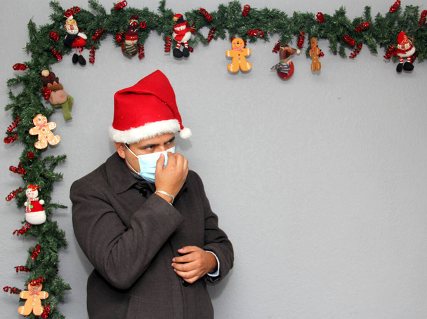 hombre latino con máscara de protección, abrigo y sombrero de Santa Claus en la decoración de Navidad, nuevo covid-19 normal - Foto, imagen