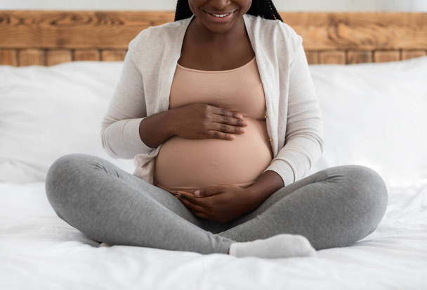 Третій триместр вагітності. Щаслива чорна очікувана жінка приймає живіт на ліжку
 - Фото, зображення