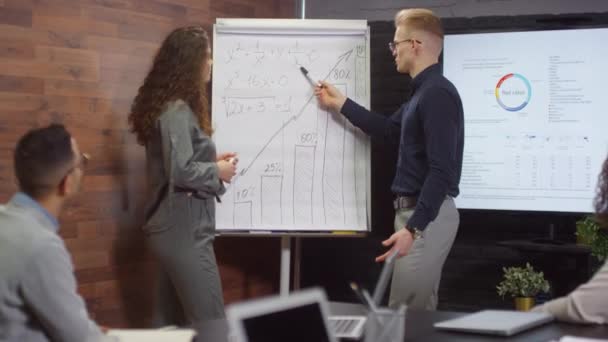 Medium shot of business meeting of young representatives of two companies discussing details of project on flipchart, making deal and shaking hands in front of partners - Footage, Video