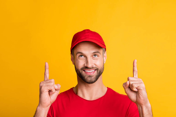 Photo of bristled man direct fingers look up empty space wear red t-shirt headwear isolated yellow color background - Photo, image