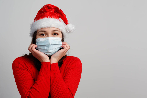 portrait of a young woman in a red Christmas cap and a protective medical mask. with copy space. - Photo, image