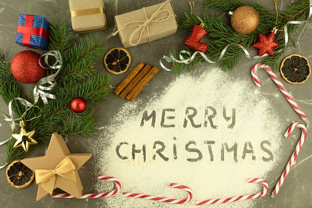 Die Inschrift auf dem verstreuten Mehl Frohe Weihnachten. Geschenke mit Süßigkeiten und weihnachtlichen Accessoires auf dem Tisch, Draufsicht. Neujahr oder Weihnachten Hintergrund mit Platz für Text - Foto, Bild