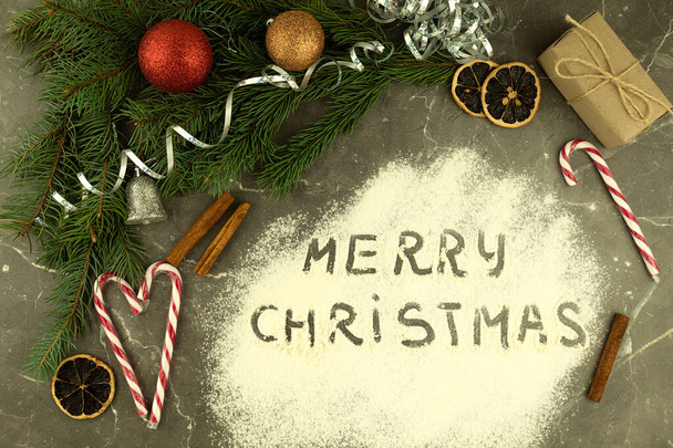 Napis na rozrzuconej mące Wesołych Świąt. Prezenty ze słodyczami i akcesoriami świątecznymi na stole, widok z góry. Nowy rok lub Boże Narodzenie tło z miejscem na tekst - Zdjęcie, obraz