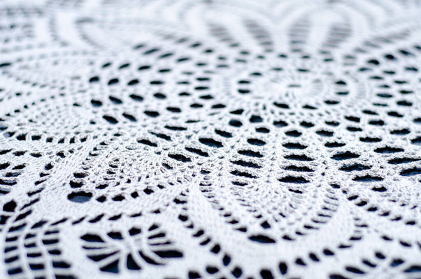 Beautiful knitted pattern close-up. Lace knitted fabric made of white thread. Handmade items. The texture is knitted from threads. - Фото, зображення