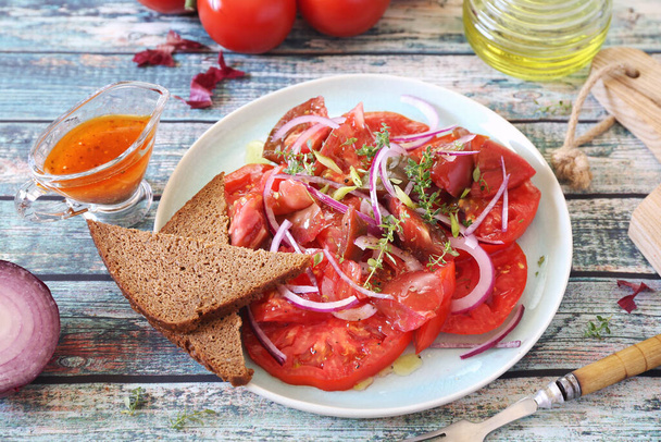 Ensalada de tomate con cebolla roja y salsa picante de diferentes variedades de tomates, dos rebanadas de pan de centeno en plato azul. Vista superior - Foto, Imagen