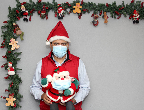 homme latin avec masque de protection et poupée santa claus dans la décoration de Noël, nouveau covid-19 normal - Photo, image