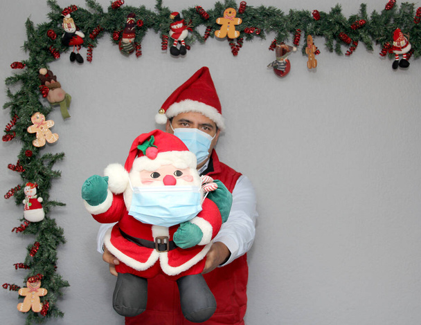 latinský muž s ochrannou maskou a Santa Claus panenkou v vánoční výzdobě, nový normální covid-19 - Fotografie, Obrázek