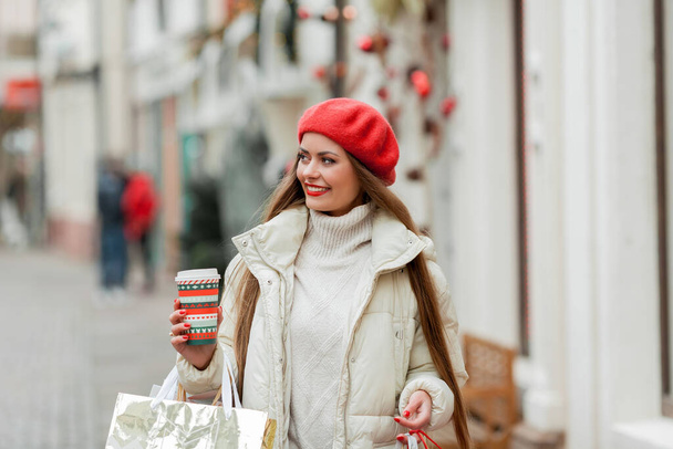 Gyönyörű fiatal nő vásárol karácsonykor. Egy vörös sapkás fiatal nő portréja egy európai város utcáin. - Fotó, kép