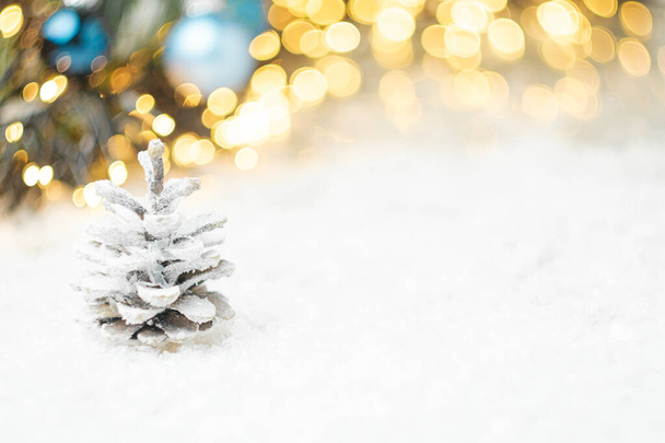 Fenyőtoboz a hóban, karácsonyi dekorációval a háttérben fénymásoló hellyel. - Fotó, kép