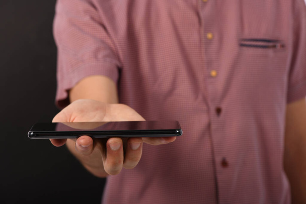 Mann hält das schwarze Smartphone mit leerem Bildschirm waagerecht. isoliert auf schwarzem Hintergrund. Foto in hoher Auflösung.  - Foto, Bild