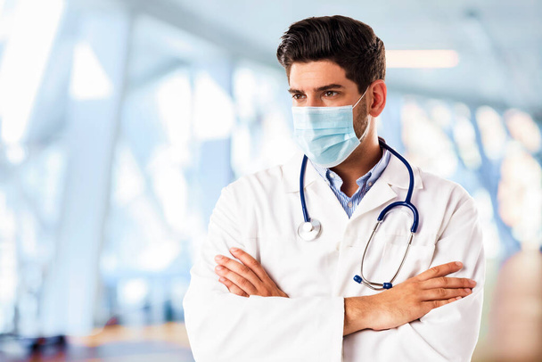 Portrait shot of male doctor wearing face mask while standing in hospitals foyer - Foto, immagini