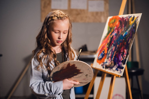 First lesson in art school, a little girl learns to draw and makes her first oil painting on canvas. - Photo, Image