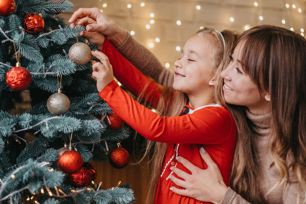 Anya és lánya együtt díszítik a karácsonyfát. Hagyományos nevelés. - Fotó, kép